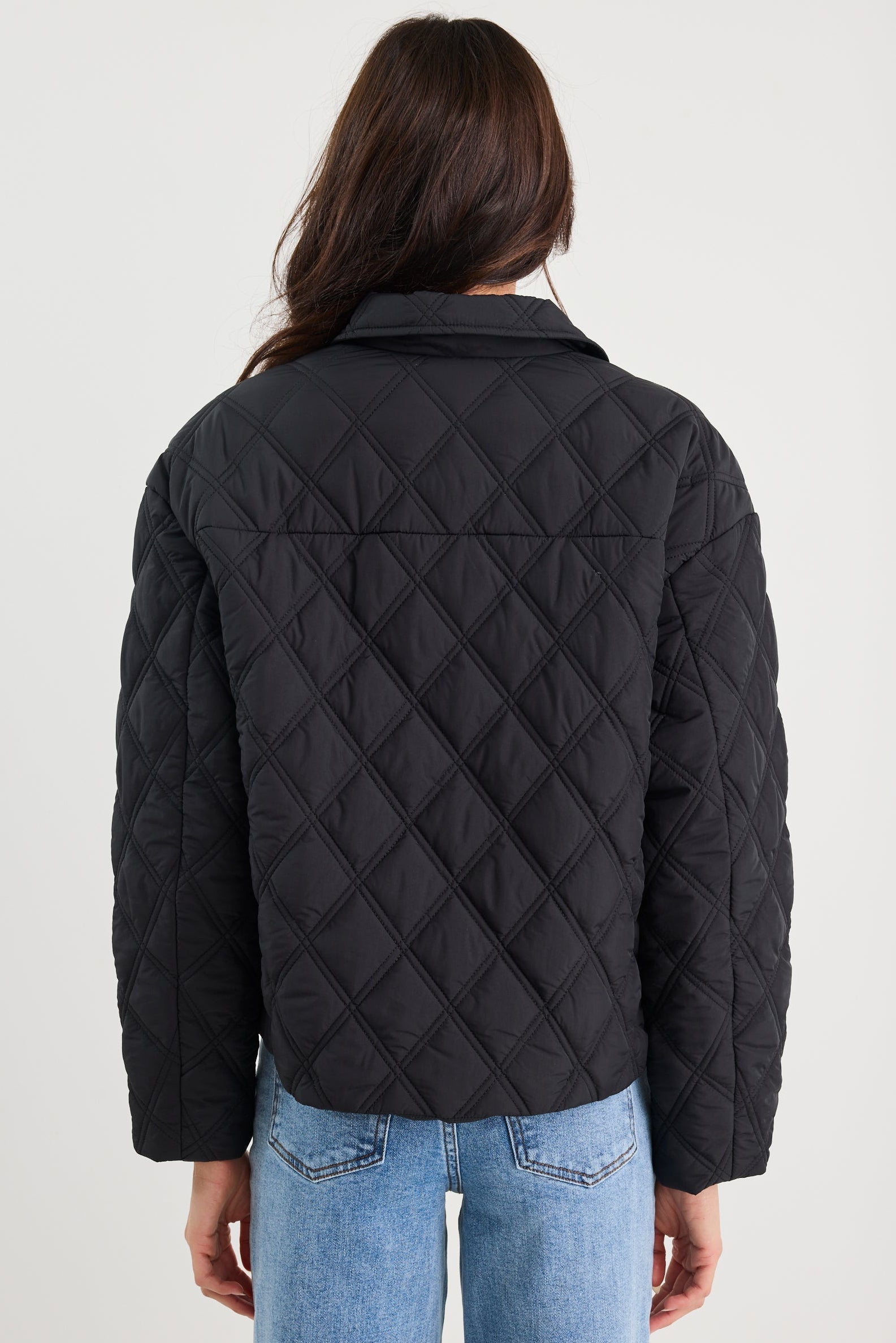 Person wearing a black quilted jacket and blue jeans on a white background
